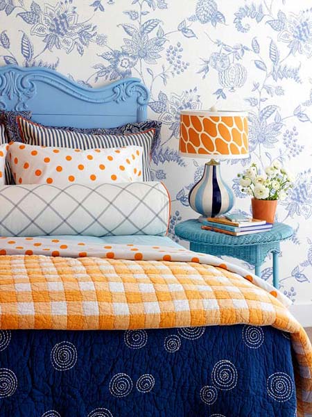 blue wallpaper pattern, blue headboard and bedside table with orange table lamp and comforter 